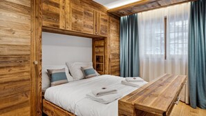 A wooden room with a bed, a wooden table, and a window with curtains. - Chalet Larchwood by Mrs Miggins 3 (Grimentz)