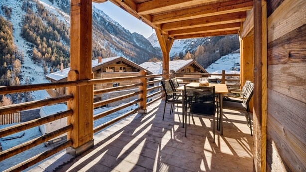A wooden balcony with a table and chairs, overlooking a snowy mountain landscape. - Chalet Larchwood by Mrs Miggins 3 (Grimentz)