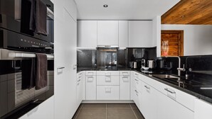 A modern kitchen with white cabinets, black countertops, and a wooden ceiling. - Chalet Larchwood by Mrs Miggins 3 (Grimentz)