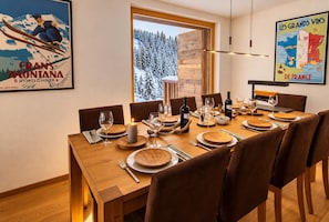 Ein Esszimmer mit Holztisch, gedeckt für sechs Personen, einem großen Fenster mit Blick auf schneebedeckte Bäume und einem Poster eines Skifahrers an der Wand.