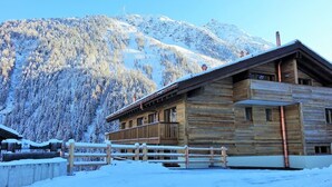A wooden cabin with a balcony, surrounded by snow-covered mountains.