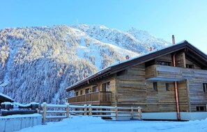 Een houten blokhut met een balkon, omgeven door besneeuwde bergen.