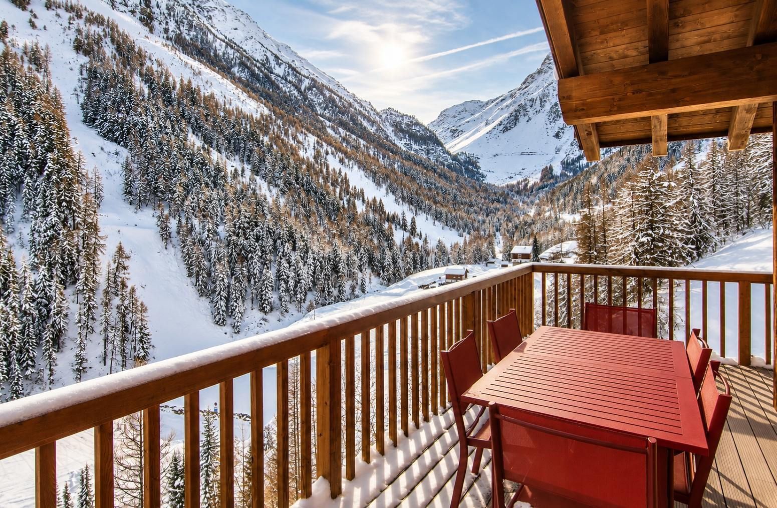 A wooden deck with a table and chairs overlooking a snow-covered mountain landscape.