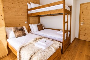 A bunk bed with white bedding and a fluffy blanket, wooden walls, and a wooden door.