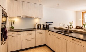 A modern kitchen with light wood cabinets, a black countertop, and stainless steel appliances.