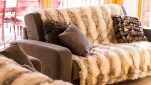 A cozy living room with a sofa covered in a striped fur blanket, a dark fur throw, and a patterned pillow.