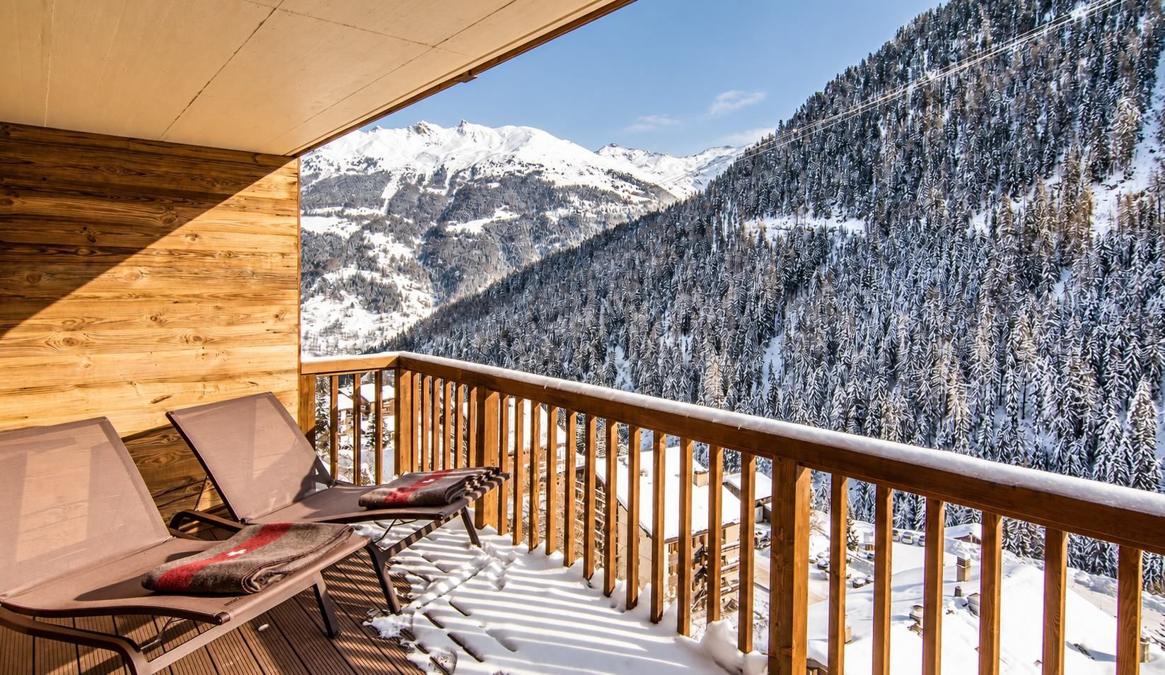 A wooden deck with lounge chairs and a view of snow-covered mountains.