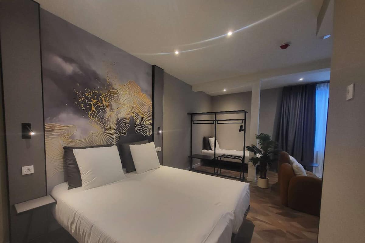A modern hotel room with a large bed, a desk, a chair, and a view of the city.
