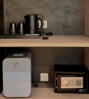 Un minibar con una cafetera, dos tazas y un control remoto. Abajo, hay un refrigerador de minibar y una caja fuerte.