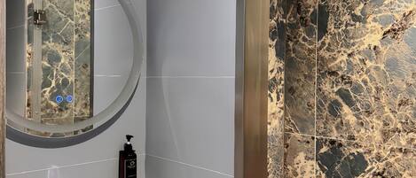 A modern bathroom with a marble shower, a sink with a faucet, and a mirror with a circular frame.