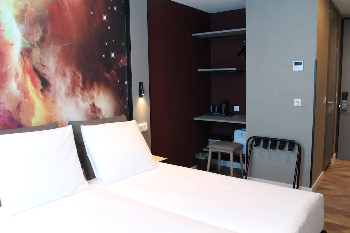 A hotel room with a bed, a desk, a chair, and a wall-mounted shelf.