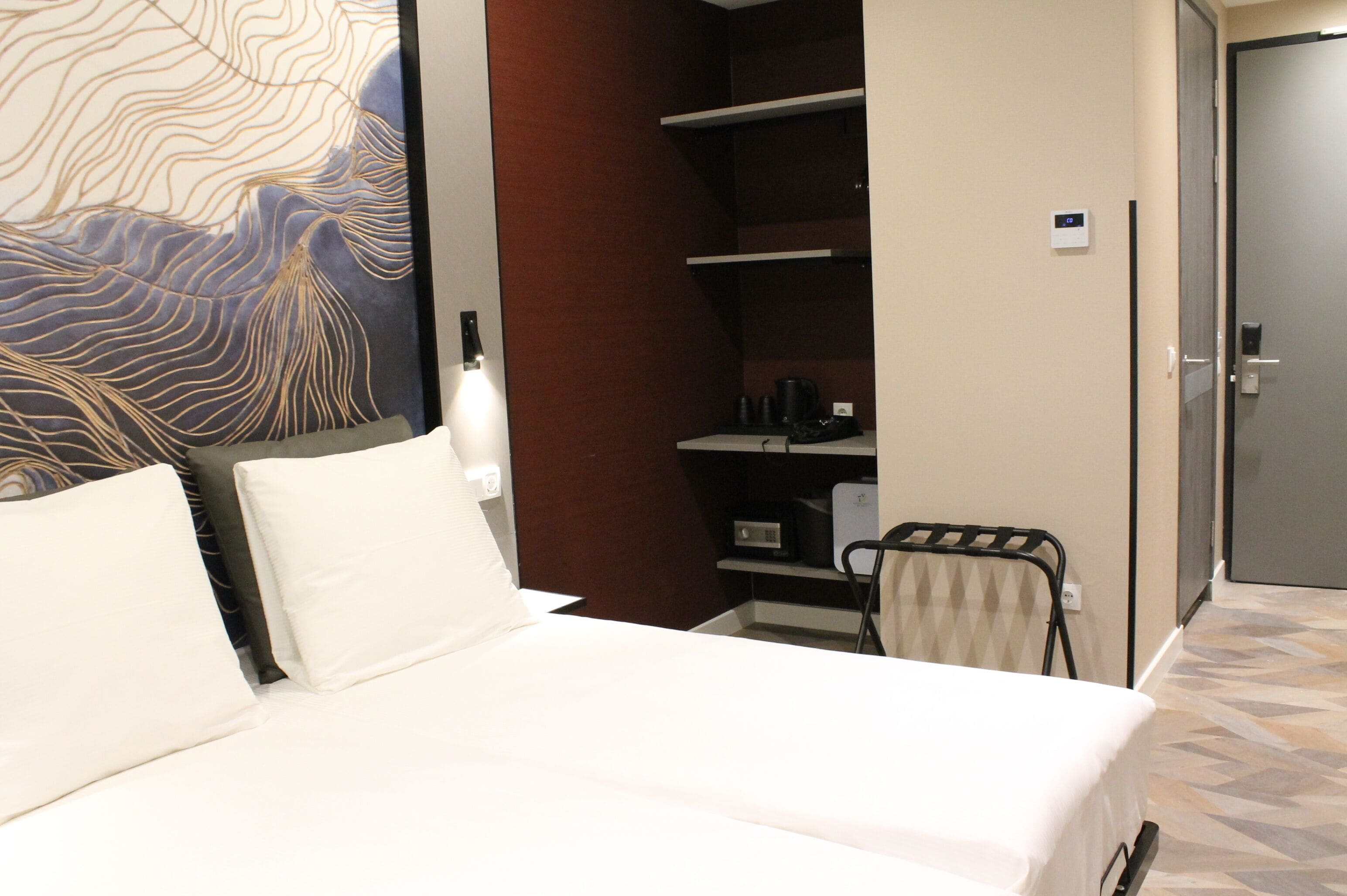 A hotel room with a bed, a wall art piece, a wardrobe, and a small seating area.