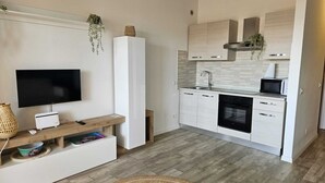 Een compacte keuken met een ingebouwde oven, magnetron en spoelbak. Een flatscreen televisie is aan de muur bevestigd boven een houten console tafel.