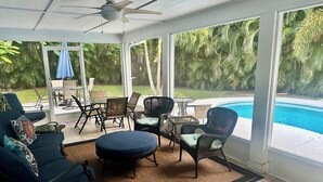 Uma sala de sol com ventilador de teto, grandes janelas e vista para uma piscina.