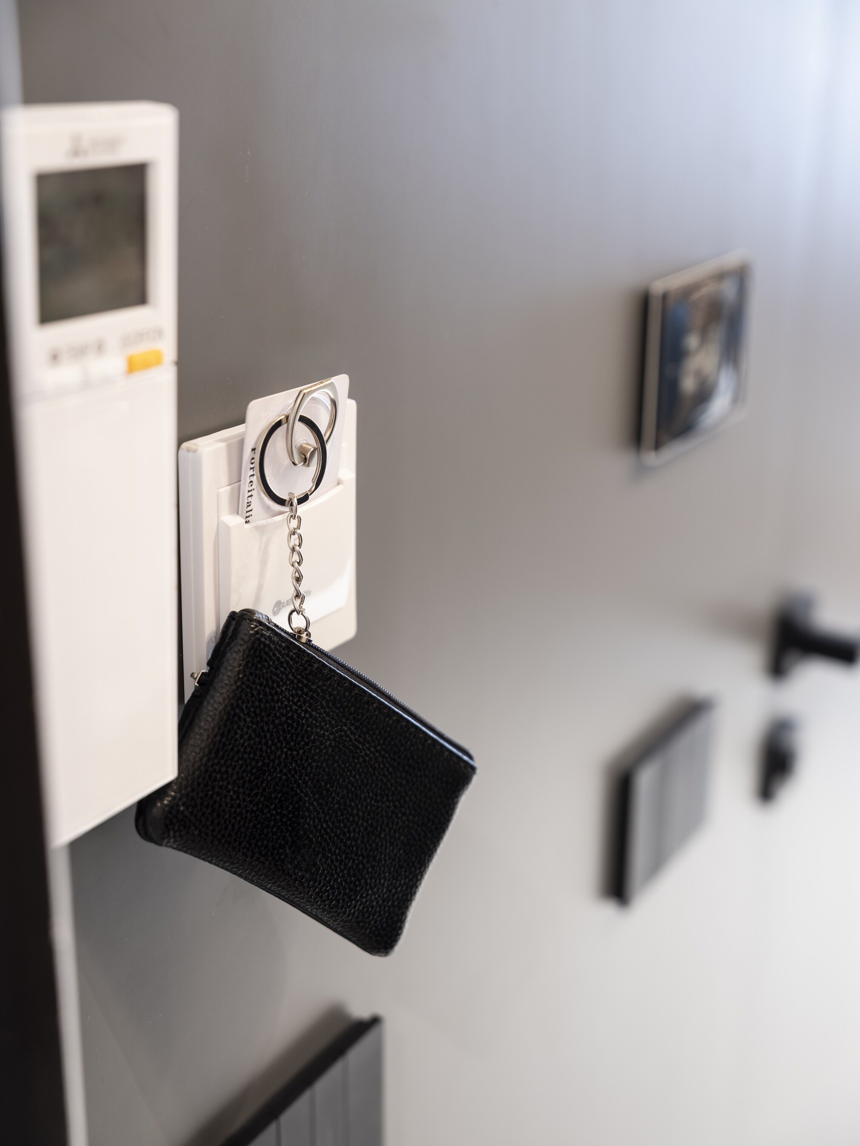 Ein an der Wand befestigter Schlüsselhalter mit einer schwarzen, strukturierten Tasche, einem kleinen weißen Gerät und einem gerahmten Bild.