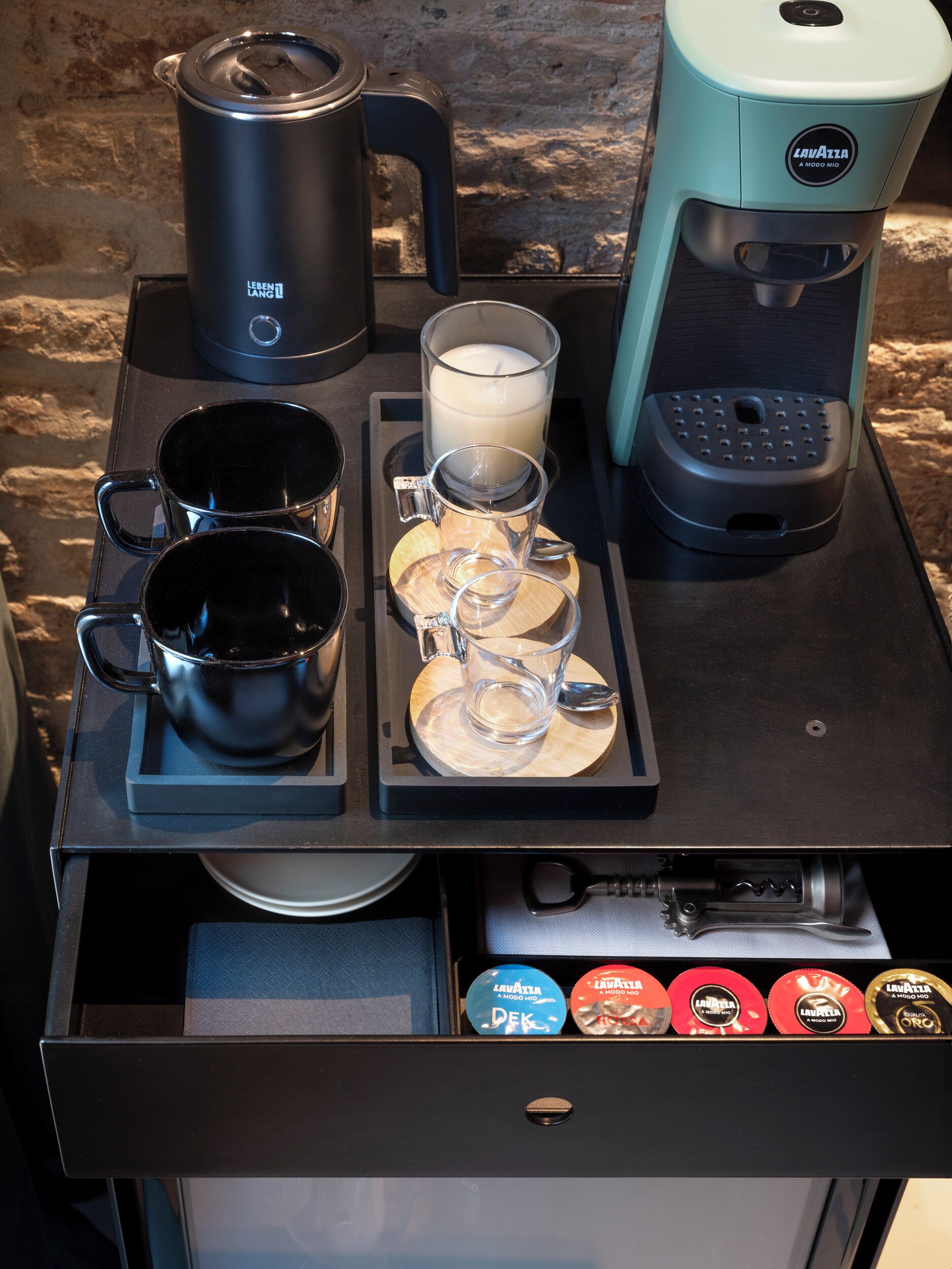 Un coin café équipé d’une machine à café, d’une bouilloire et d’un plateau avec des tasses et une bougie.