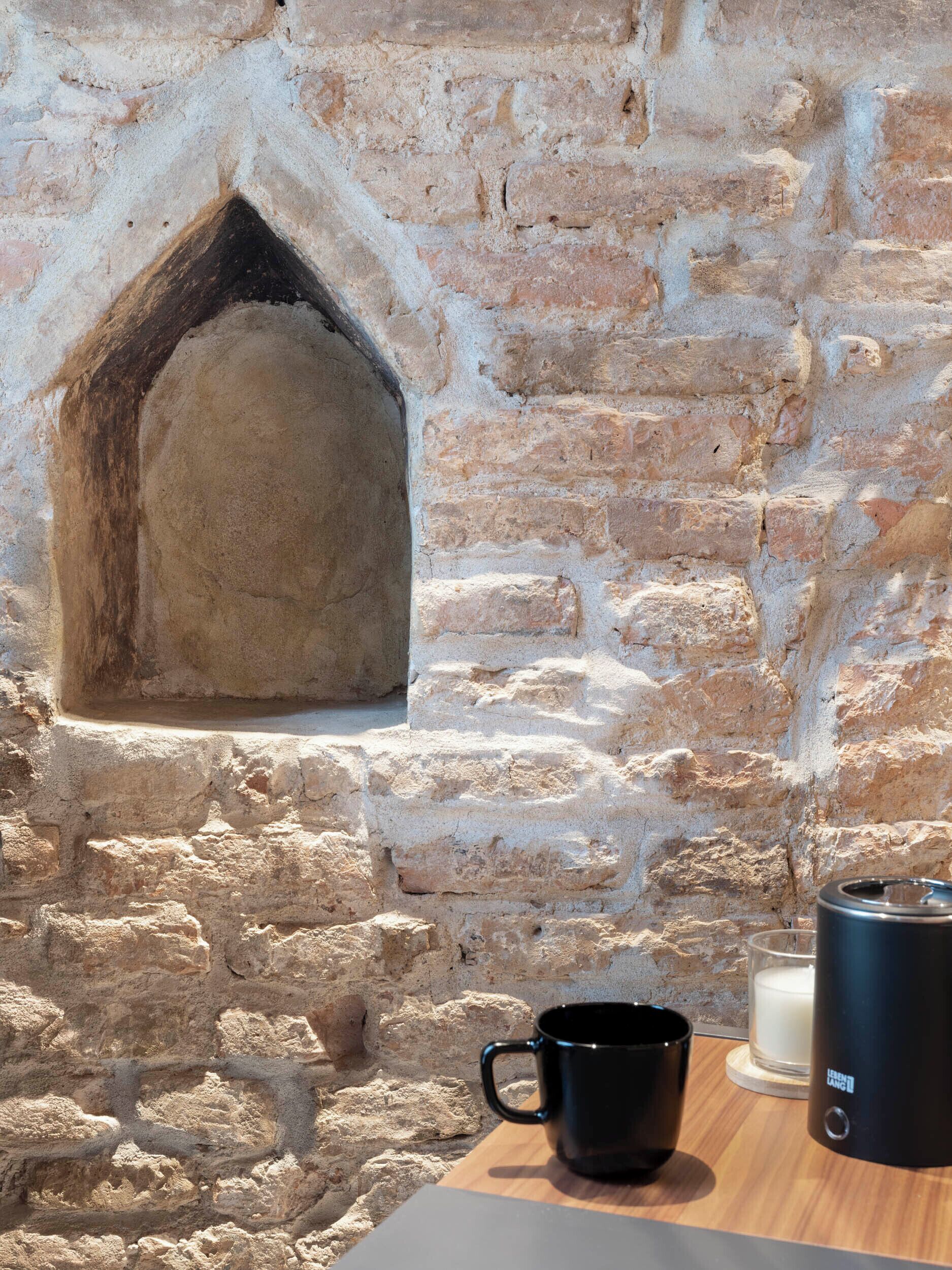 A stone wall with a fireplace, a black mug, and a candle on a wooden table.