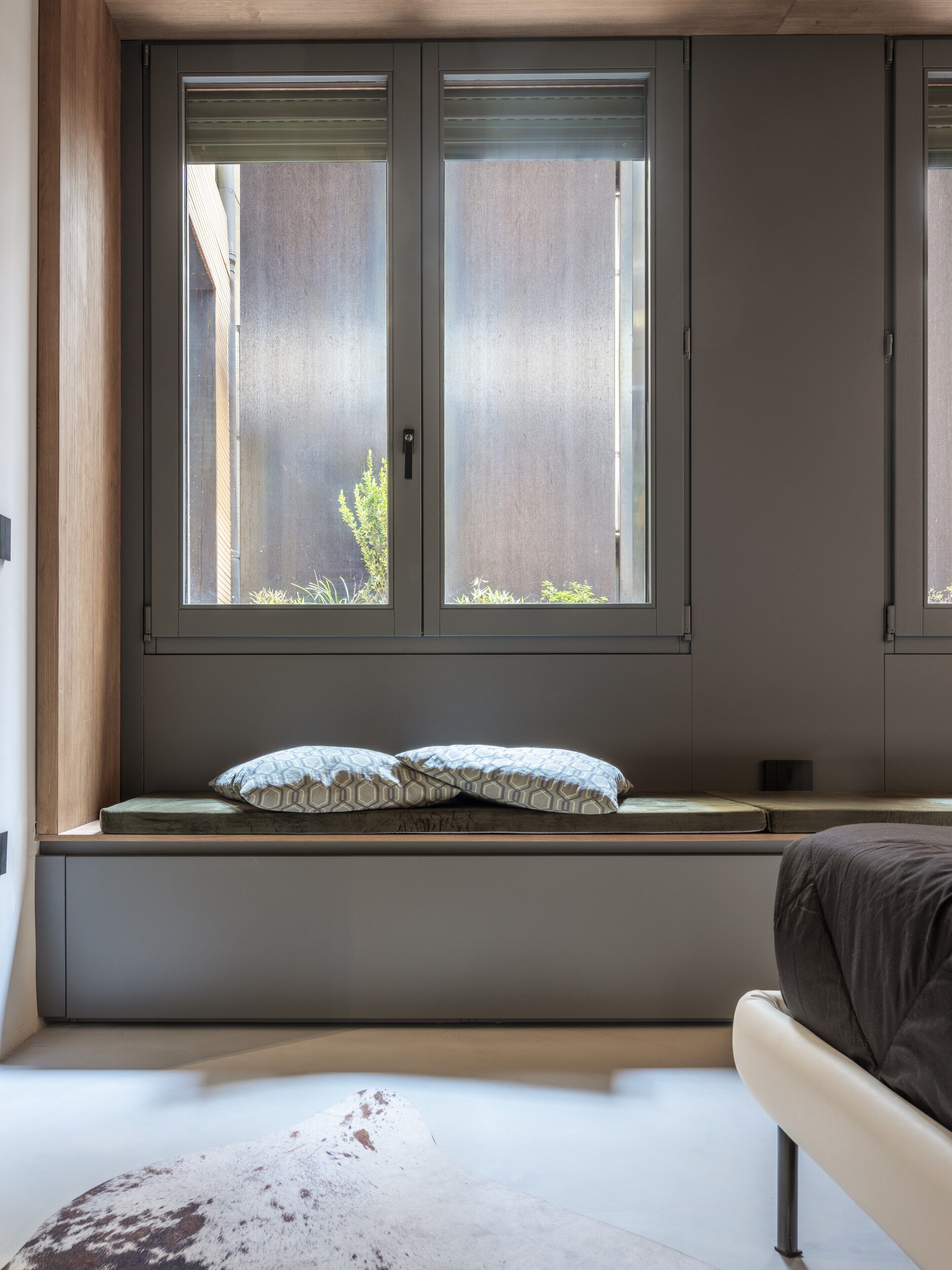 A bedroom with a bed, a window seat with cushions, and a view of the outside.