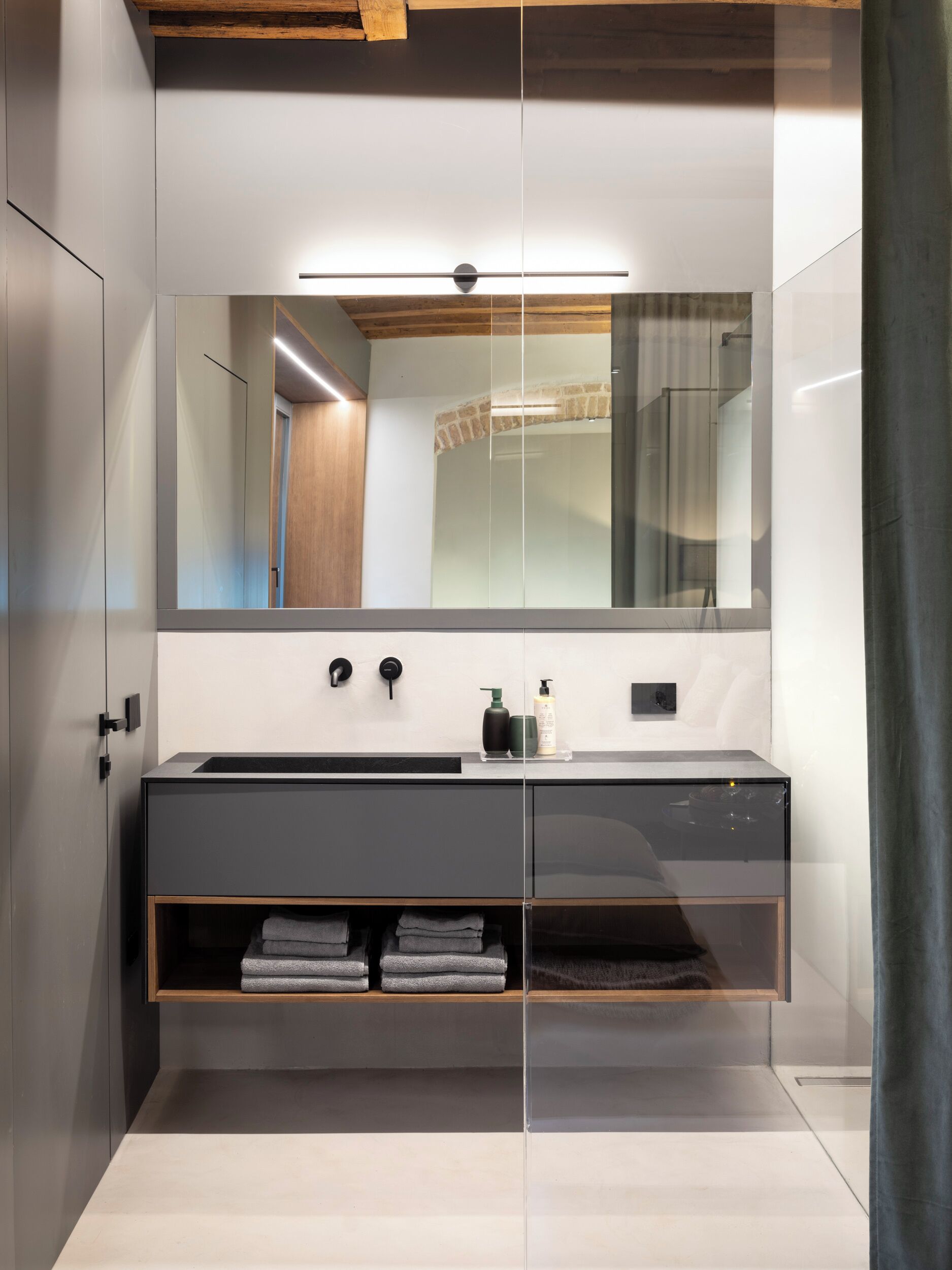Un baño moderno con tocador separado por vidrio, espejo y toallero empotrado.