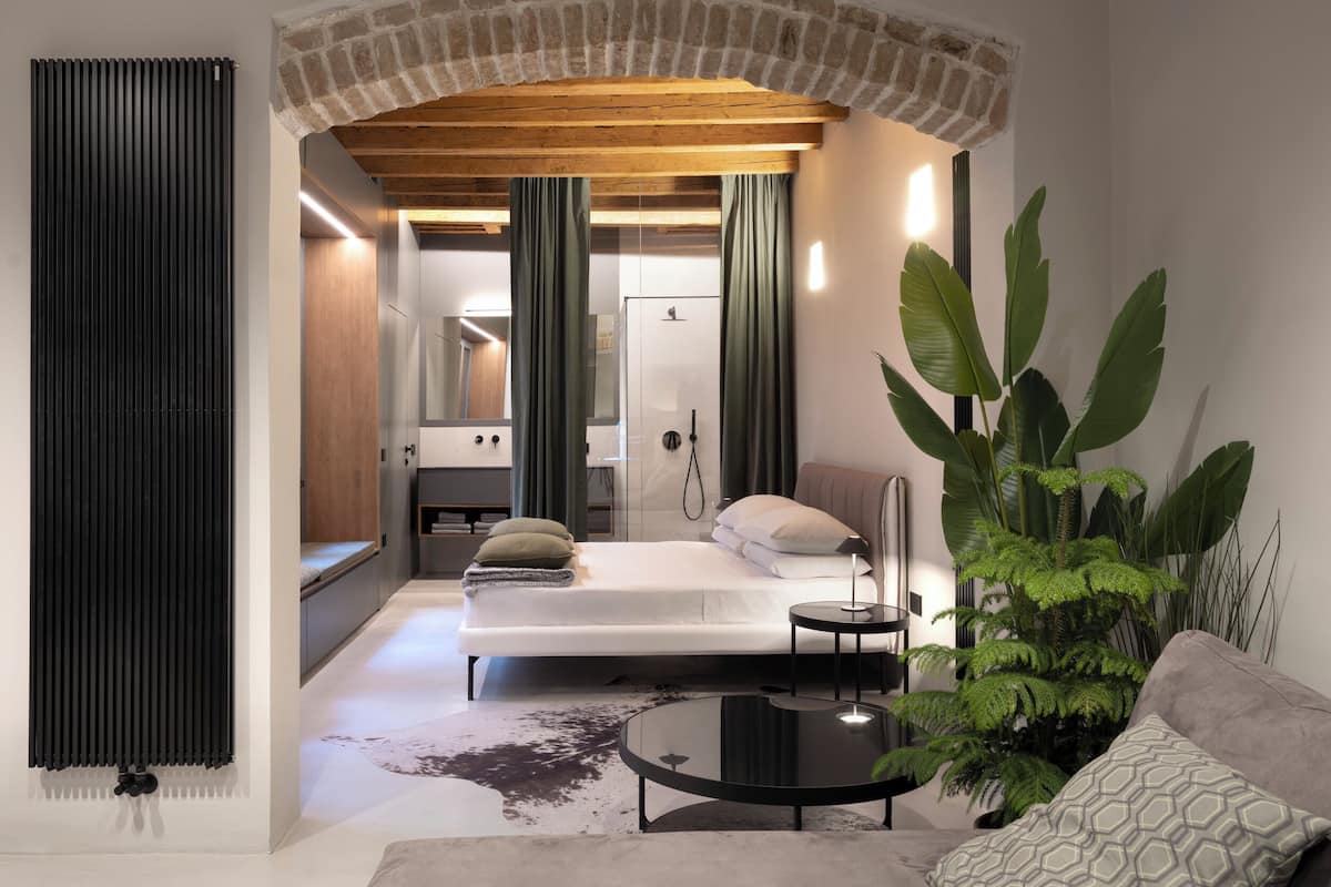A compact bedroom with a bed, bedside tables, a mirror, and a large potted plant.