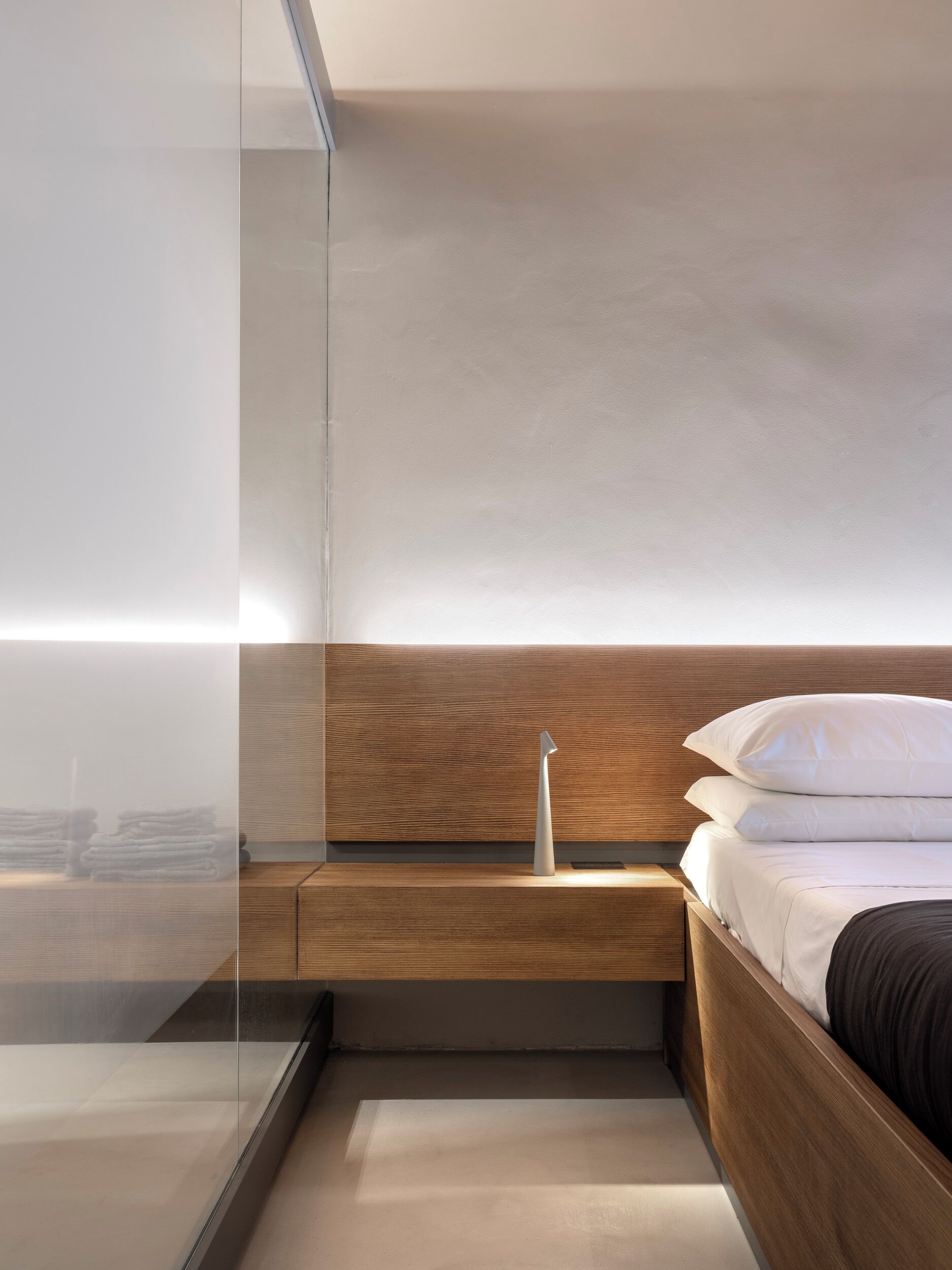 Un dormitorio moderno con cabecera de madera, mesita de noche y cama con ropa de cama blanca y oscura.