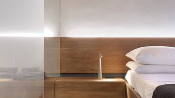 Un dormitorio moderno con cabecera de madera, mesita de noche y cama con ropa de cama blanca y oscura.
