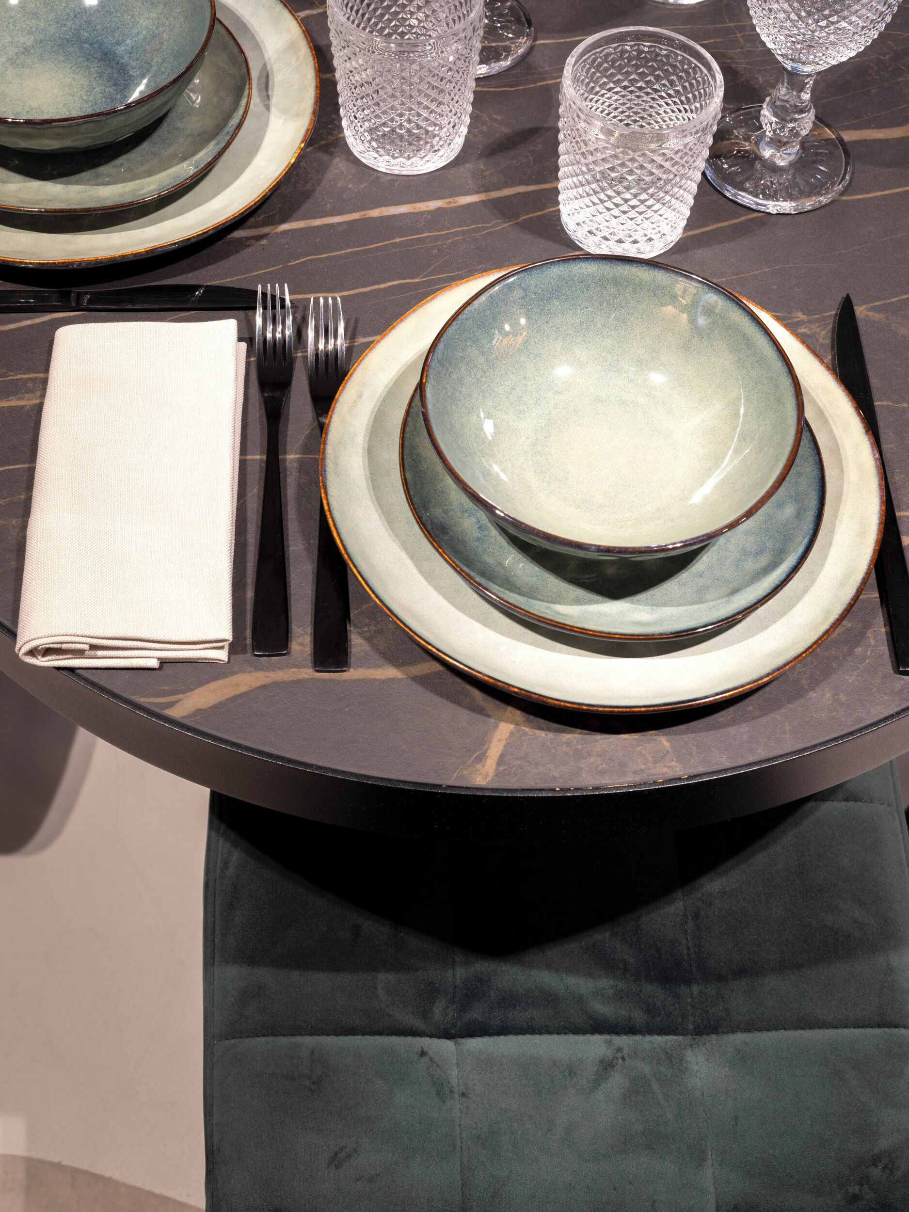 A table set with plates, bowls, glasses, cutlery, and a folded napkin.