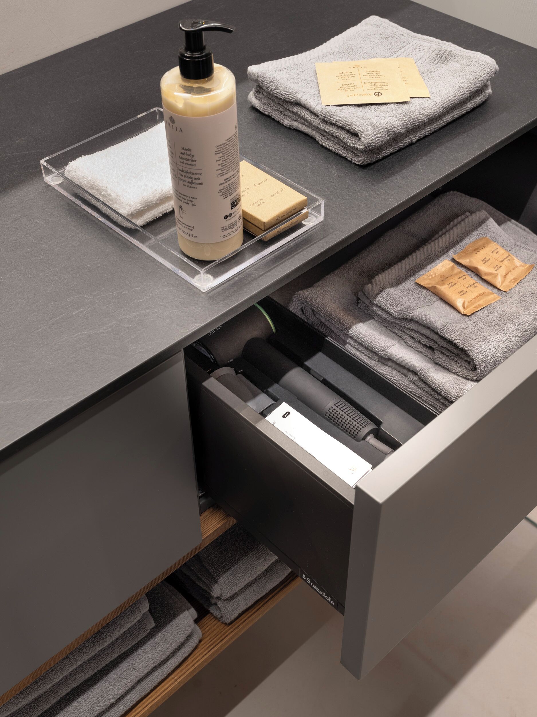 Une salle de bain avec un comptoir gris, un flacon de savon liquide, une serviette pliée et un porte-serviettes.