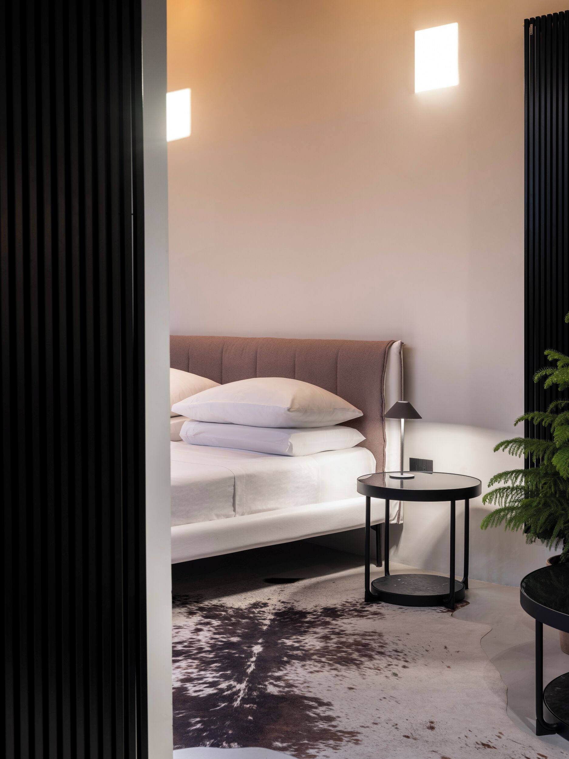 Un dormitorio moderno con cama, mesita de noche, lámpara y planta en maceta.