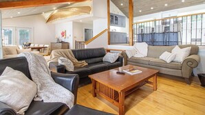 Un salon spacieux avec un plafond en bois, un canapé en cuir noir, un canapé beige et une table basse en bois.