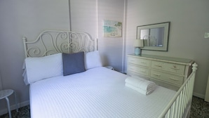 A neatly made bed with a white headboard and pillows, a bedside table with a lamp, and a dresser with drawers. - Vintage Modern GEM in the Heart of Santurce w/parking (San Juan)
