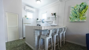 A compact kitchen with a central island, white bar stools, and a large green leaf painting on the wall. - Vintage Modern GEM in the Heart of Santurce w/parking (San Juan)