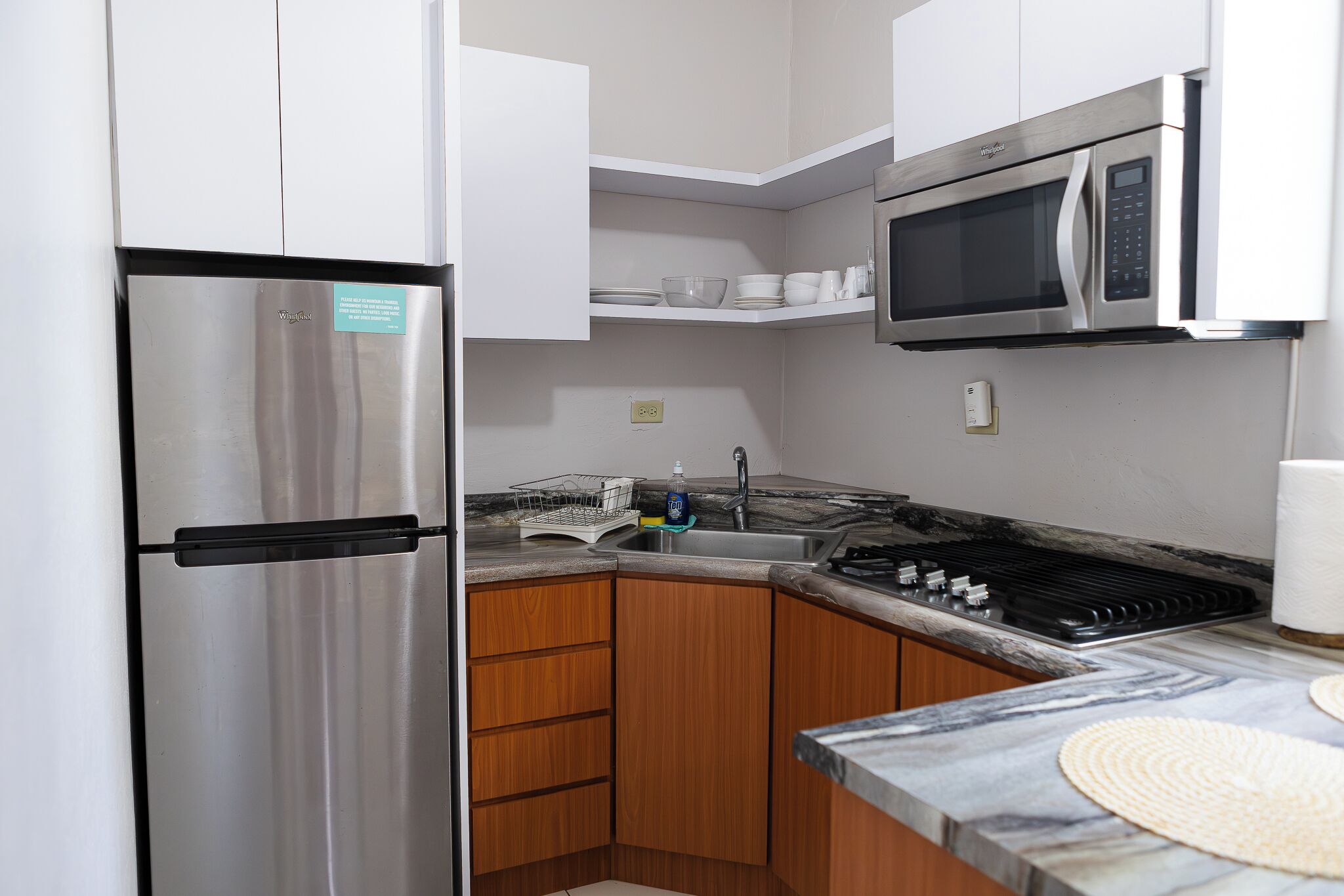 Une cuisine compacte équipée d’un réfrigérateur en acier inoxydable, d’un four à micro-ondes, d’une cuisinière et de meubles de rangement en bois.