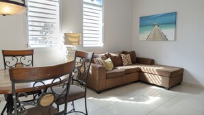 Ein Wohnzimmer mit einem braunen Sofa, einem Esstisch mit Stühlen und einem Gemälde eines Piers an der Wand.