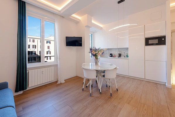 A modern kitchen with white cabinets, a built-in oven, and a dining area with a white table and chairs.