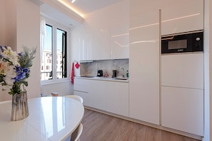 A modern kitchen with white cabinets, a built-in oven, and a window with a view of buildings.