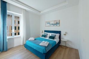 A bedroom with a bed, a window with curtains, a bedside table, and a wall-mounted artwork.