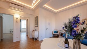 Un soggiorno moderno con un tavolo bianco rotondo, un vaso decorativo e una bottiglia di vino. C'è un divano blu e un piccolo tavolino con una lampada.
