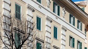 Un edificio a più piani con persiane verdi e dettagli architettonici classici.