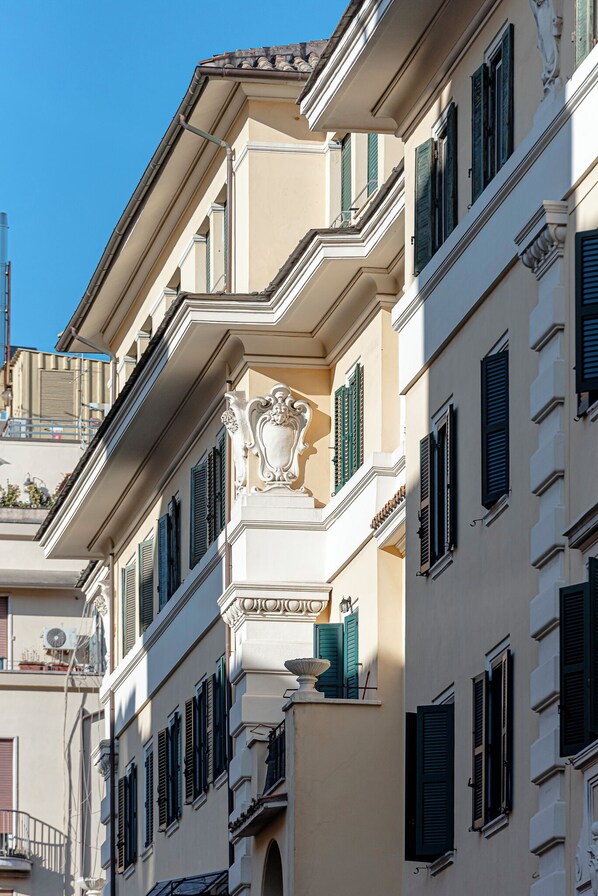 A multi-story building with balconies, green shutters, and classical architectural details.
