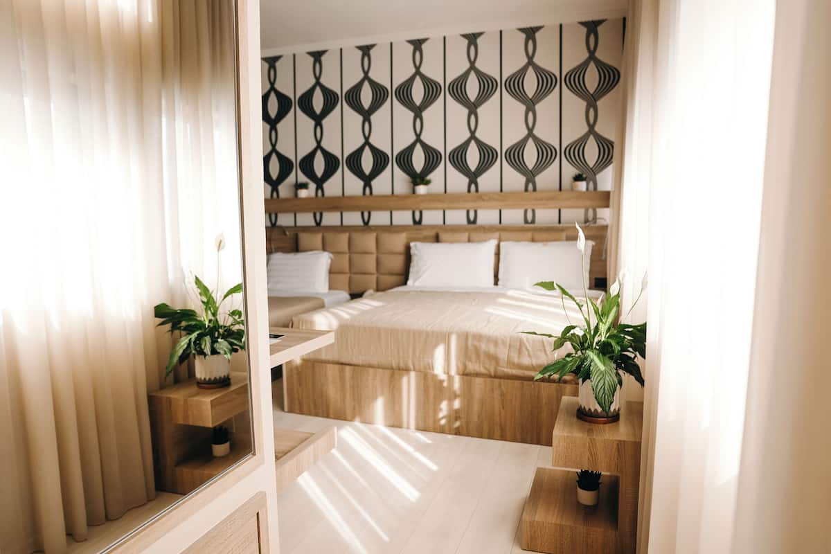 A modern hotel room with a large bed, wooden headboard, and two potted plants.
