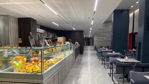 Een modern restaurant met een glazen vitrine vol fruit en een zithoek met tafels en stoelen.