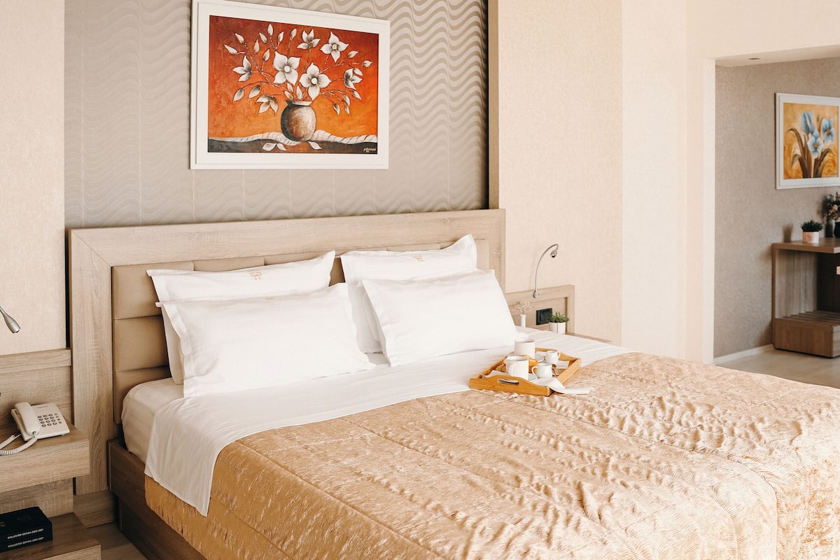 A bedroom with a large bed, a wooden headboard, a painting on the wall, and a bedside table with a lamp.