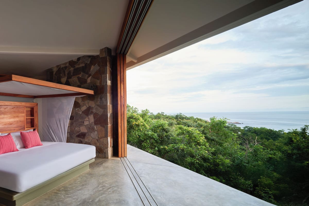 Une chambre avec un lit, un mur en pierre et une vue sur l’océan.