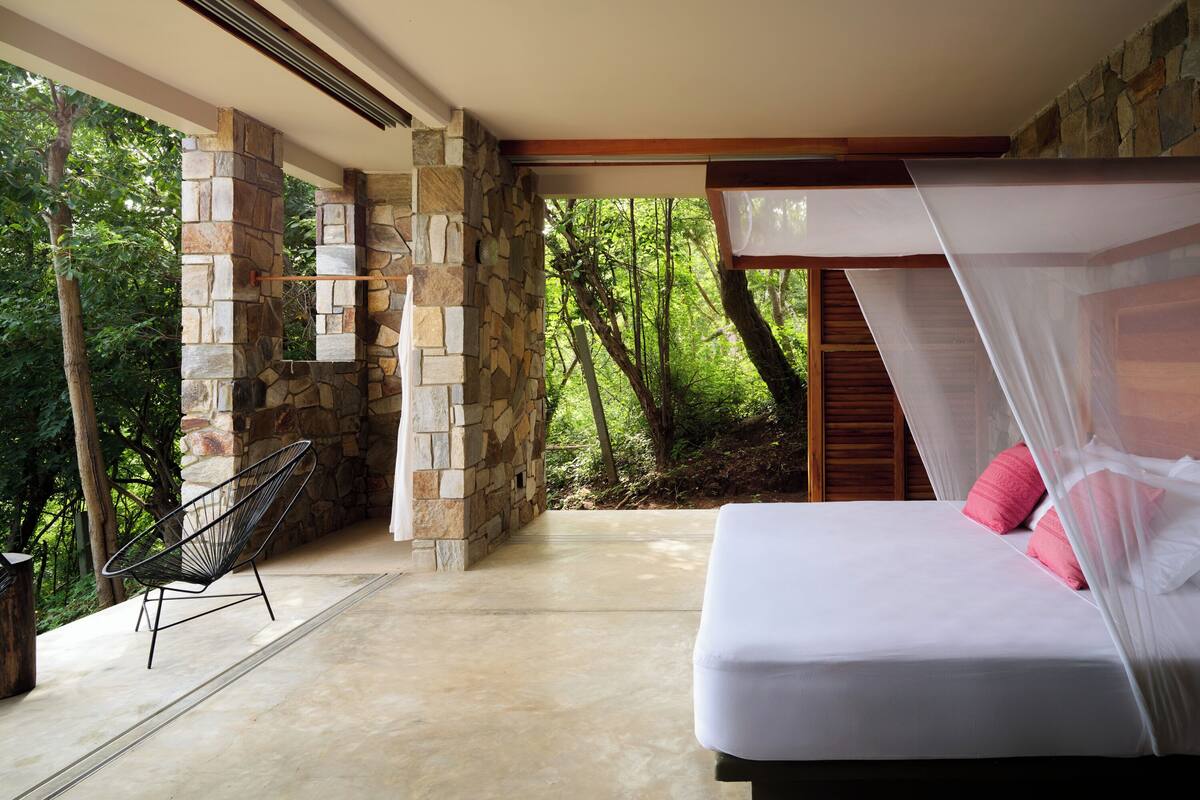 Une chambre avec un mur en pierre, un lit à baldaquin et une vue sur une forêt.