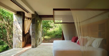 Un dormitorio con pared de piedra, cama con ropa de cama blanca y roja, y vista a zonas verdes al exterior.