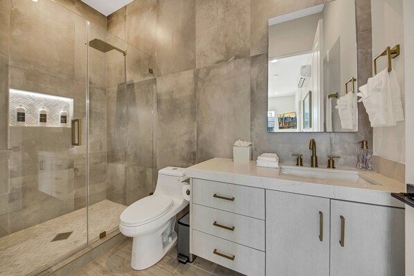 A modern bathroom with a glass-enclosed shower, a white toilet, and a vanity with gold handles. - Empire State 7br, Golf, Waterslide, Gamerm (Indio)