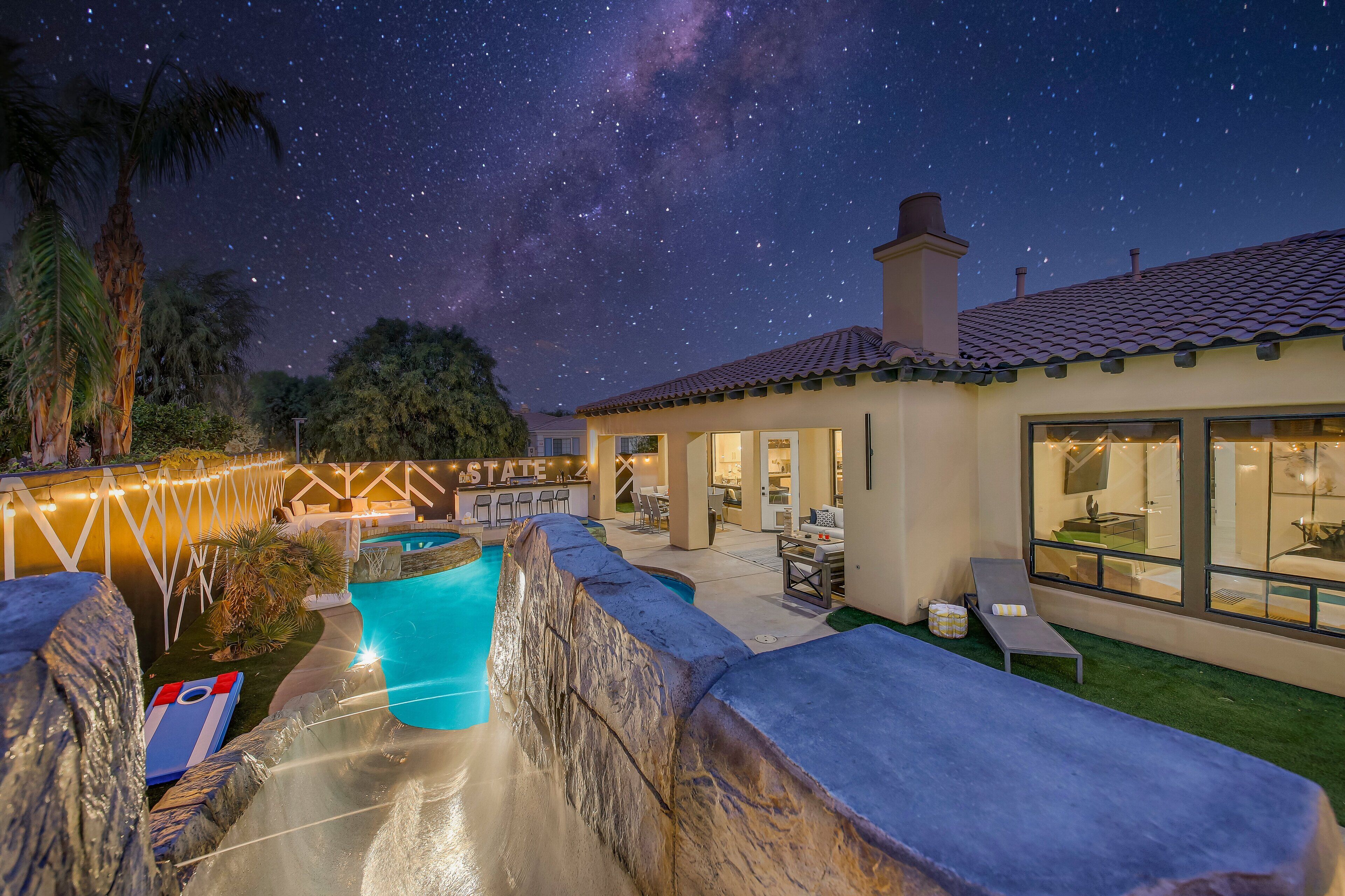 A backyard with a swimming pool, a stone waterfall, and a patio area with outdoor furniture.