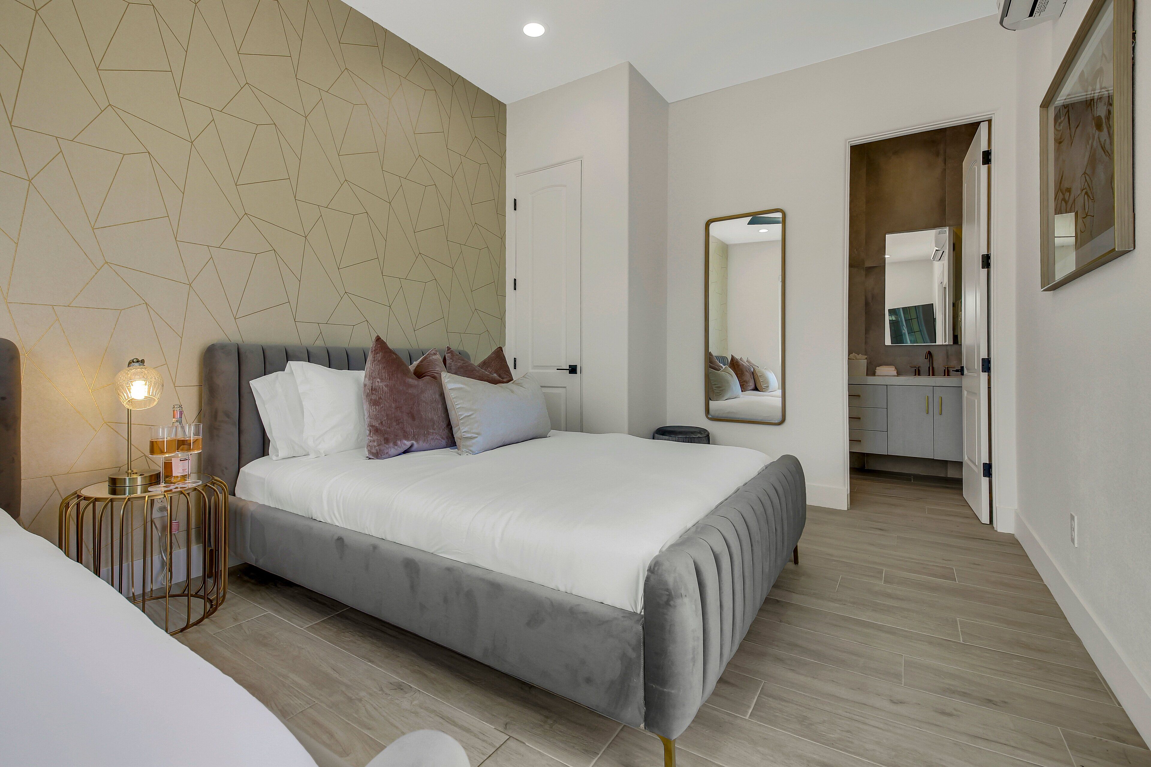 Een moderne slaapkamer met een groot bed, nachtkastjes, een spiegel en uitzicht op de badkamer.