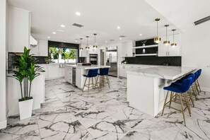 Uma cozinha moderna com piso de mármore, armários brancos e banquetas azuis.
